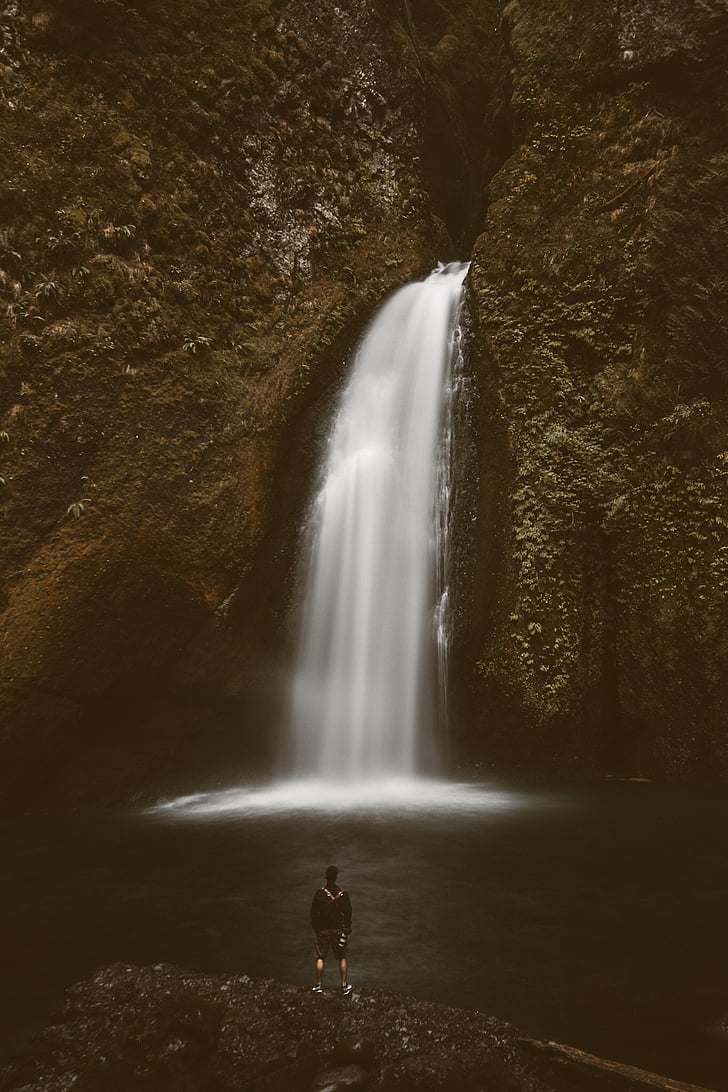 man in black jacket standing near waterfalls