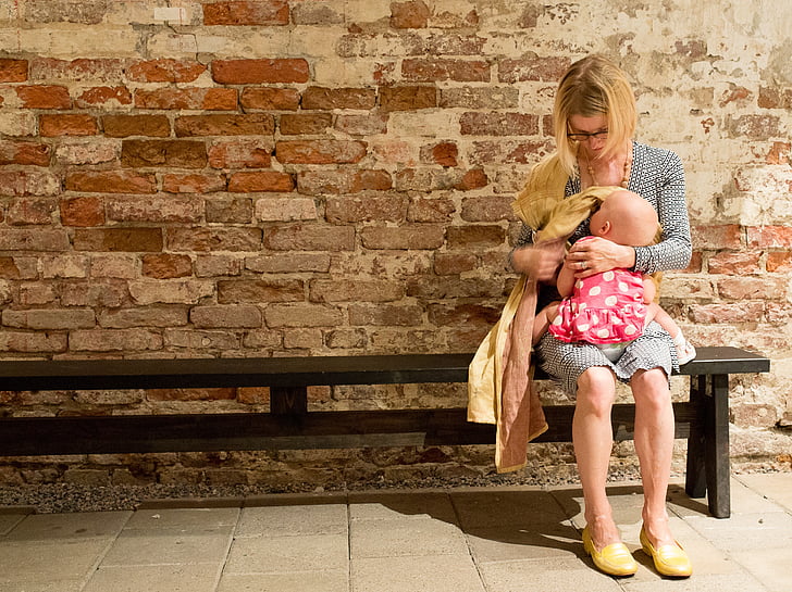 woman carrying baby and sitting on bench