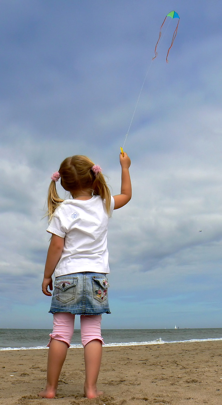 girl holding string of kite flying under white cloudy sky near seashore at daytime