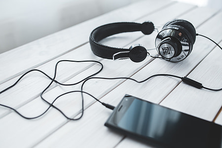 photo of black corded headphones beside smartphone on table
