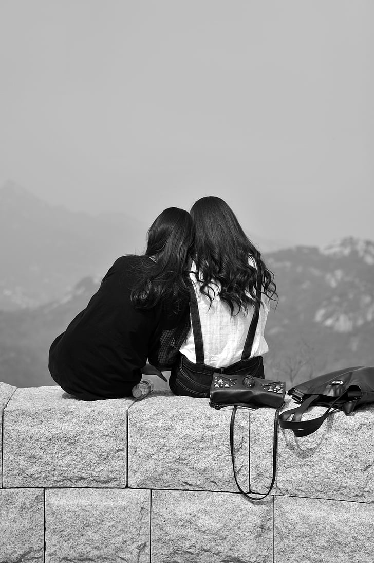 grayscale photo of two women sitting on cinder block wall