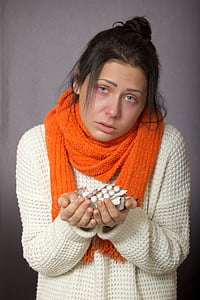 woman wearing sweater and scarf holding medication tablets