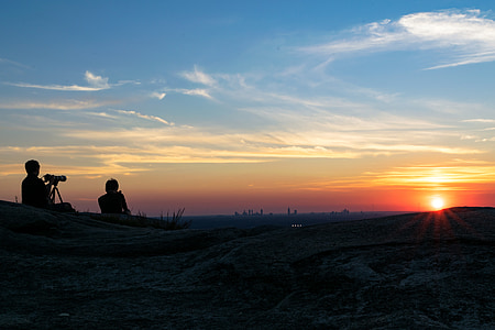 two man sitting on ground with camera during sunset