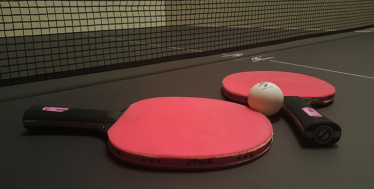 Royalty-Free photo: Two red ping pong paddles beside of white ball