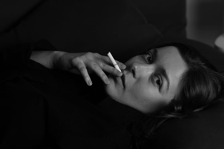 grayscale photo of lying woman while smoking