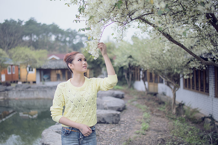 woman wearing green knitted sweater holds white flower at daytime