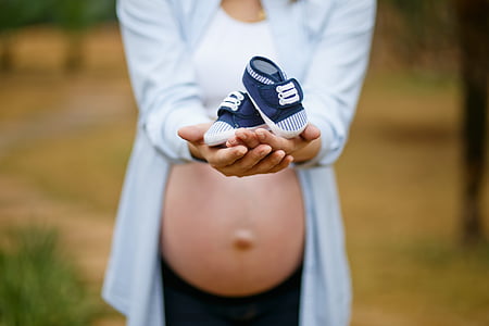 pregnant woman holding baby's blue shoes