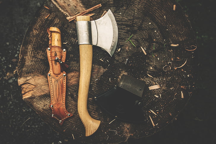 brown and silver hatchet beside brown leather knife sheath on wood stump