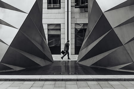 grayscale photo of man walking beside building