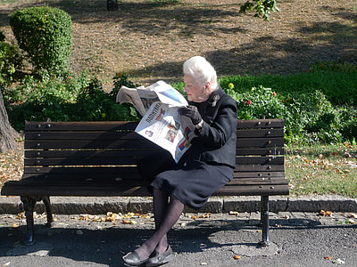 woman sitting on bench reading newspaper at daytime