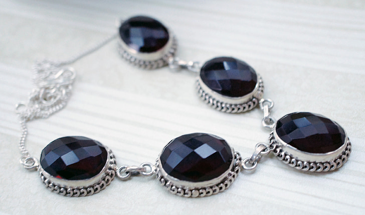 silver-colored black gemstone studded necklace on beige surface