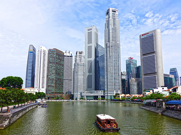 brown and white boat on water near grey high rise buildings under blue and white cloudy sky