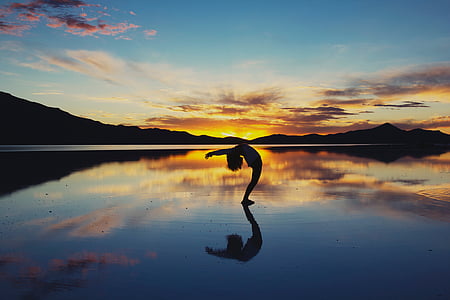 silhouette photo of person bending on body of water against orange sky