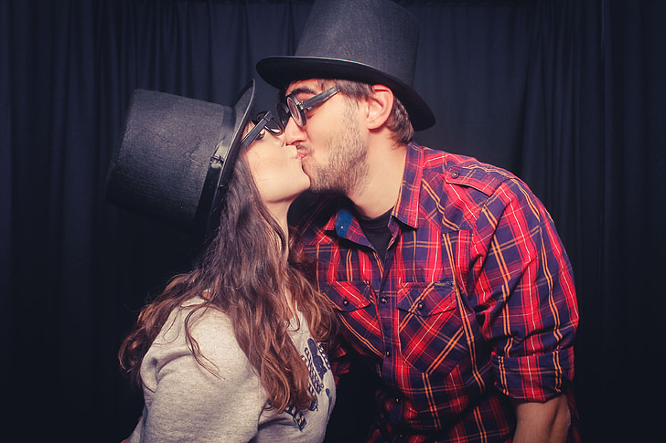 man kissing woman wearing black hats