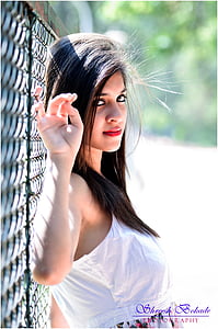 woman wearing white sleeveless top leaning on chain link barrier