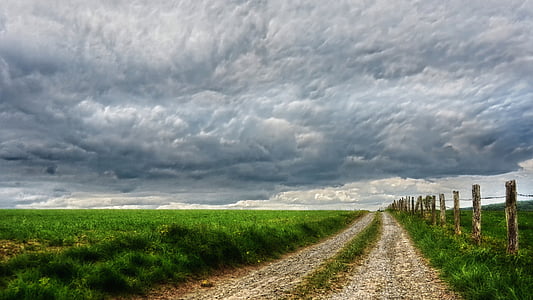empty road between grass field under cloudy sky at daytime
