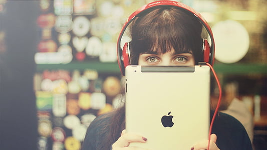 selective focus photography of woman wearing red corded headphones while holding silver iPad