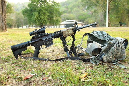 black assault rifle with scope beside gray tactical vest on green grass field photo