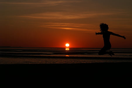 woman taking jump shot at beach during dusk