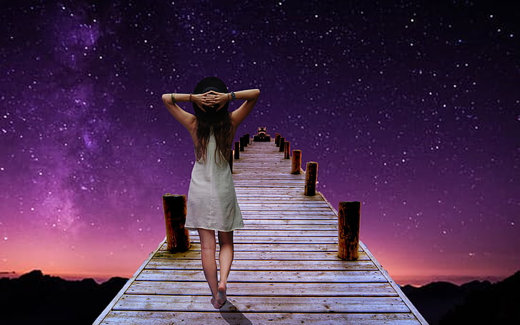 woman holding the back of her head while walking on dock during nighttime