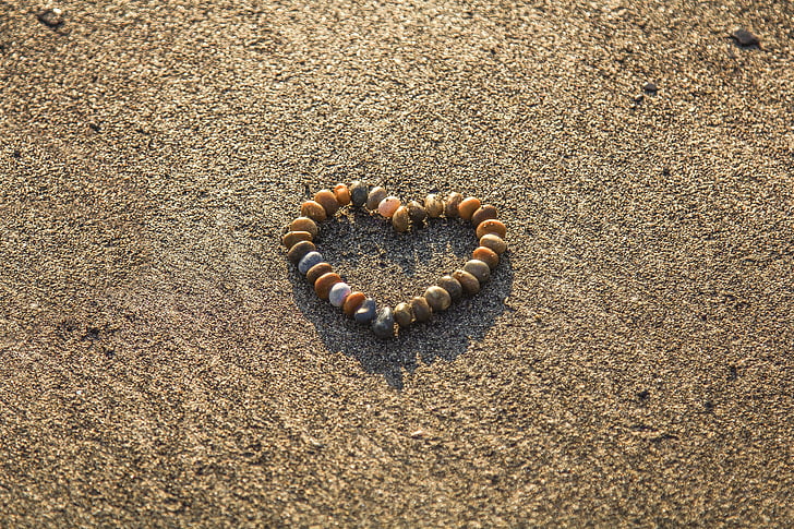 beaded brown, white, and green heart bracelet on gray sand