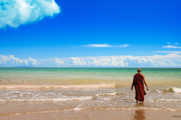 man in red robe standing on beach shore during day time
