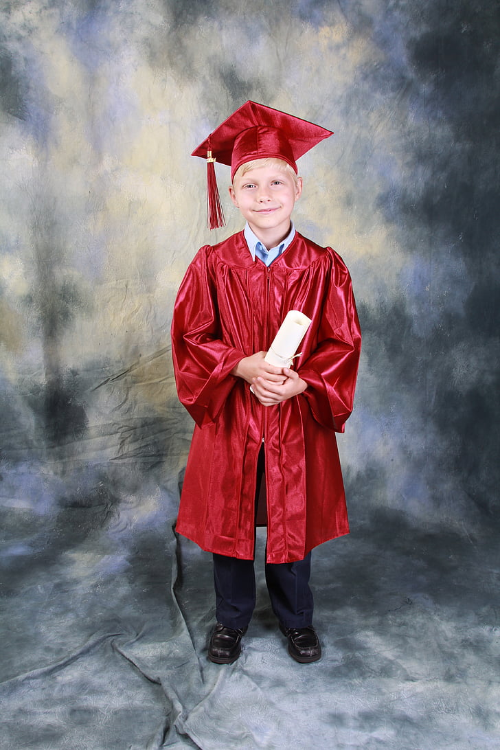 boy in red academic gown holding diploma while standing