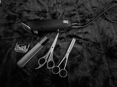 grayscale photography of corded hair clipper and trimming shears on textile