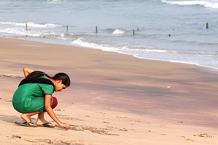 woman in green sari dress writing on sand in front of shore