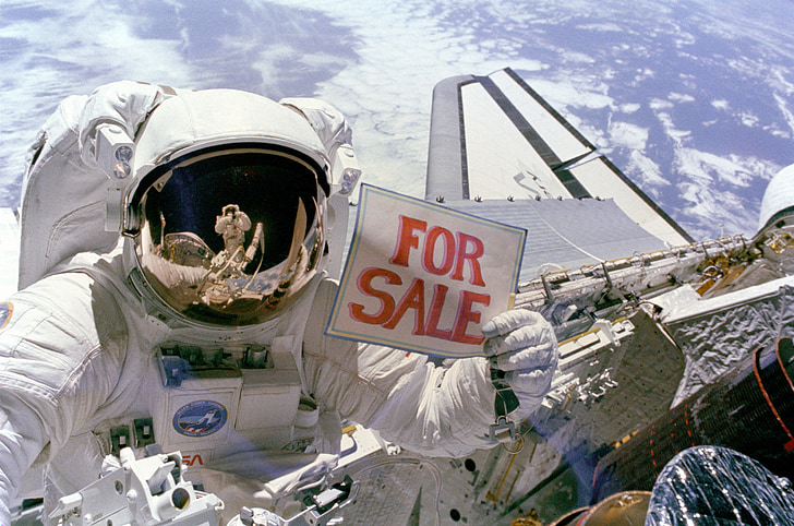 person wearing astronaut suit holding For Sale signage photography