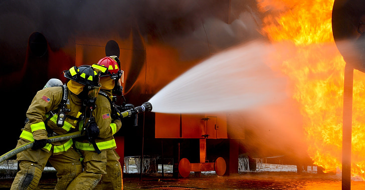 two fireman holding fire hose with water splashes on flame