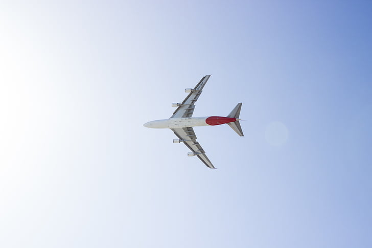 low-angle photography of white and red plane on mid-air under blue and white sky during daytime