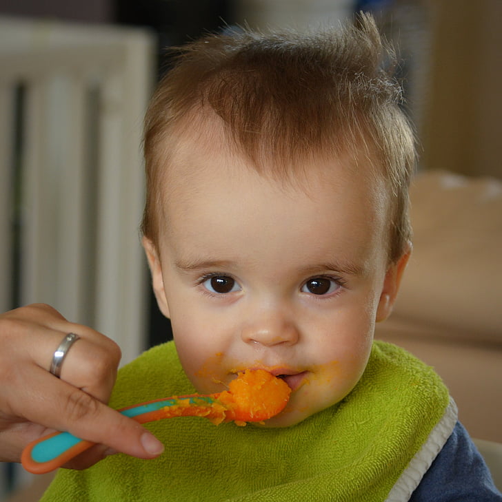 person's left hand holding food filled feeding spoon at baby's mouth