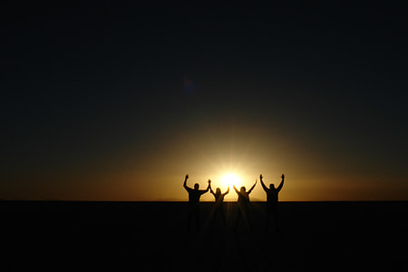silhouette of four person raising hand during sunset