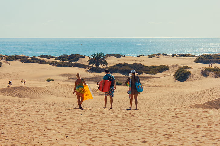 three people walking on brown sand near sea at daytime