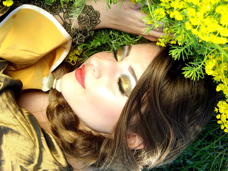 close-up photography of woman in gold-colored eyeliner lying on green grass field