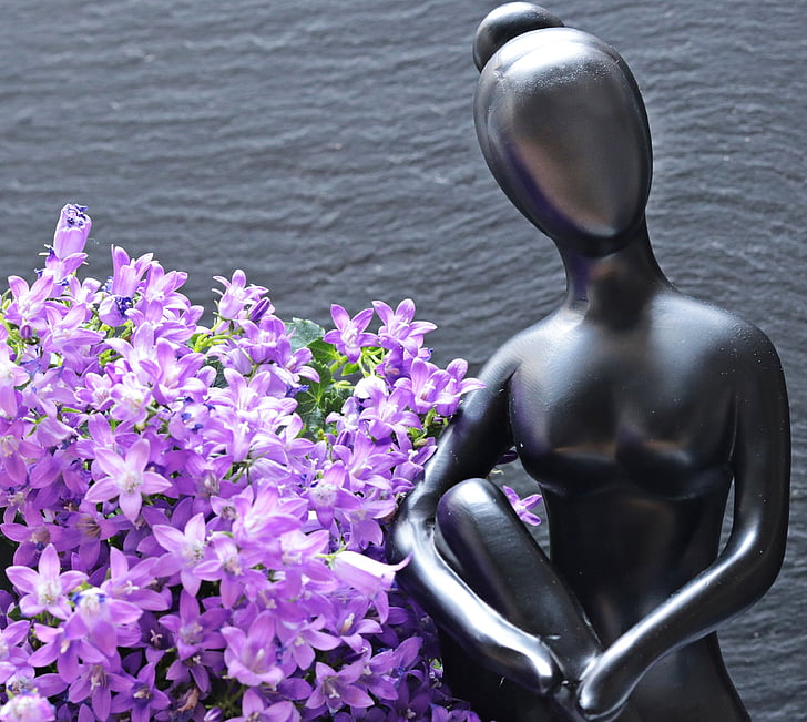 gray metal woman figurine beside purple flowers