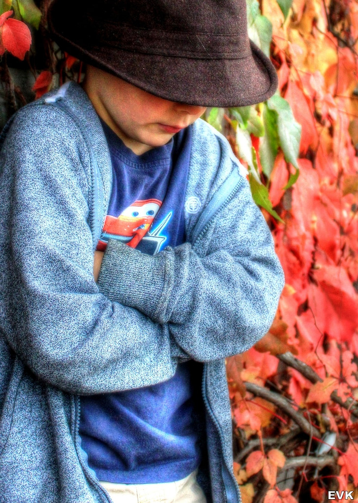 shallow focus photography of boy in black hat and blue cardigan