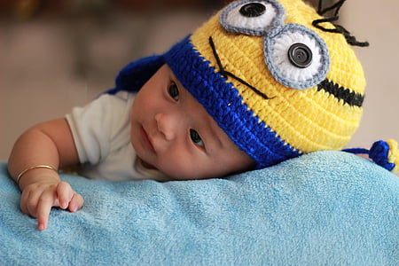 baby boy laying on blue cloth wearing Minion chullo hat