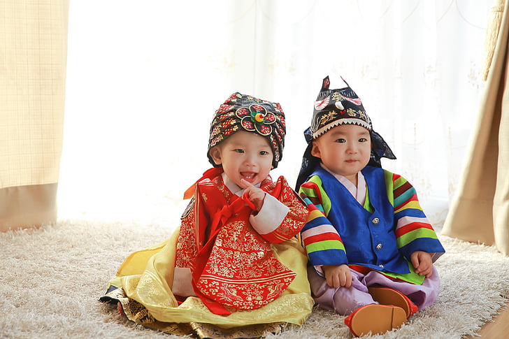 two children in traditional clothes sits on white fleece rug