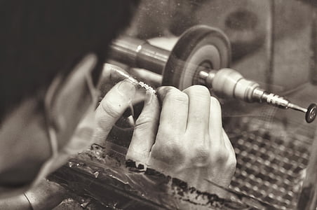 grayscale photography of man cleaning jewelry with bench grinder
