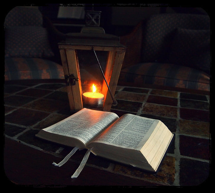 open book near candle lantern inside room