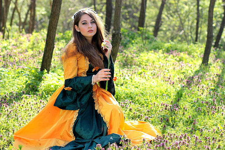 woman in orange and green long-sleeved dress sitting in the woods during daytime