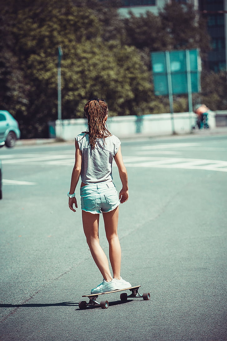 selective focus photography of girl wearing grey cap-sleeved shirt and blue denim shorts skateboarding