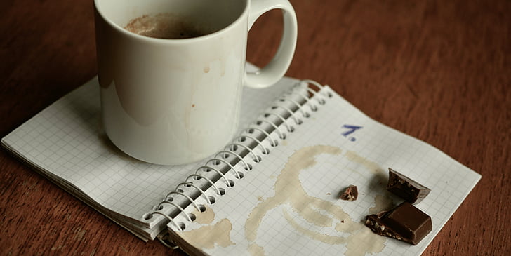 white ceramic mug and chocolate placed on notebook page