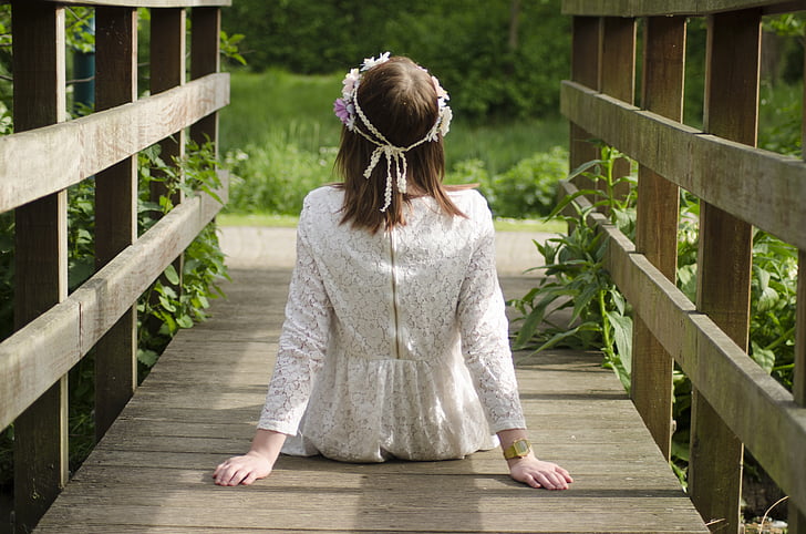 woman wearing white long-sleeved top sitting on brown wooden bridge