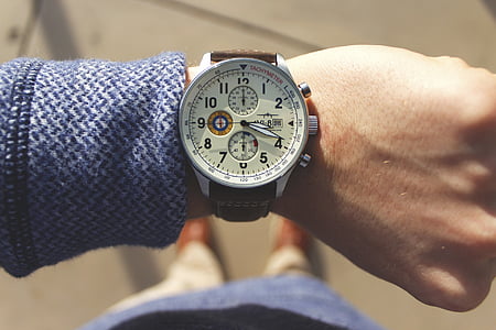 person wearing round silver-colored chronograph watch with brown leather band