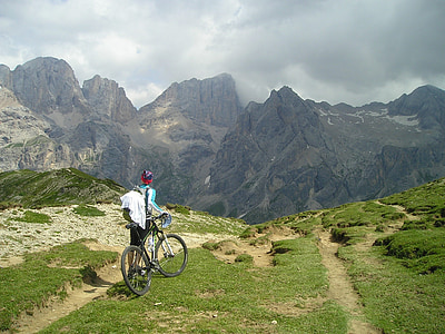person holding full-suspension bike on top of mountain under white clouds during daytime