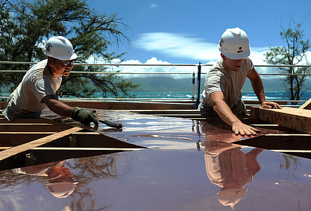 two men placing brown roof sheets on brown wooden panel