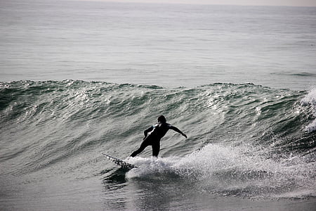 grayscale photography of person riding surfboard on barrel waves